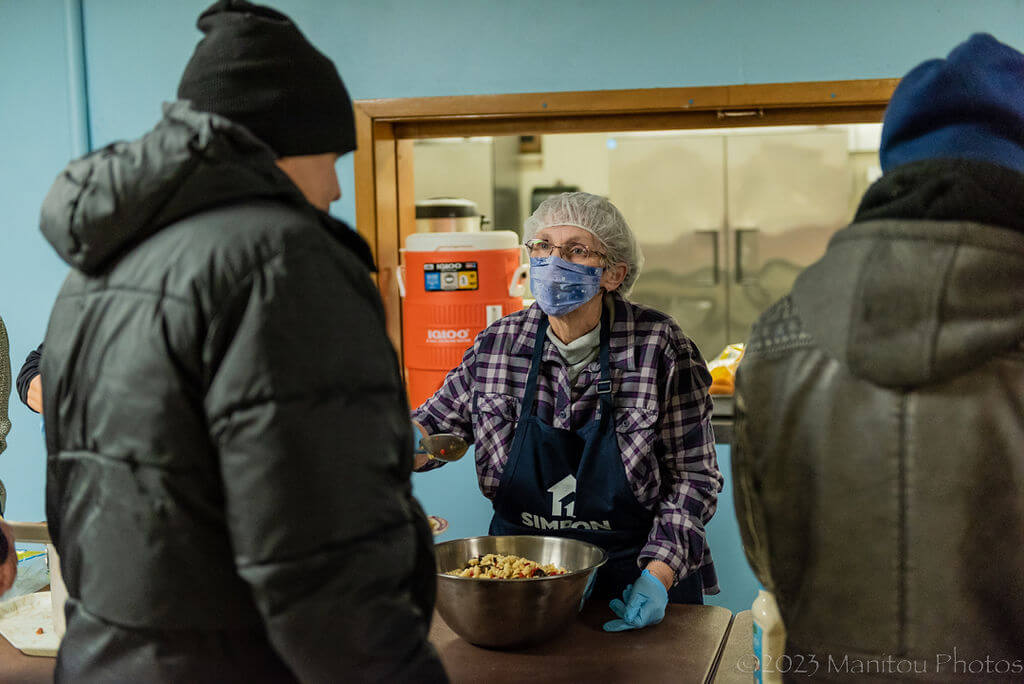 Img: A woman serves a meal to shelter guests